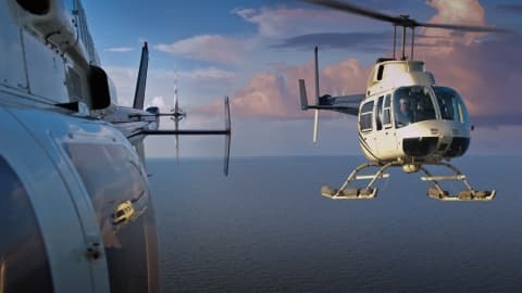 Two helicopters in flight over open water