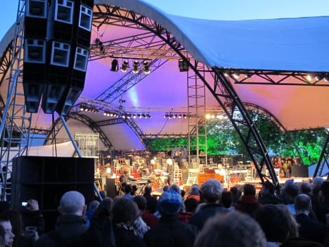 Outdoor concert stage at dusk with line array speakers, stage lighting and crowd in the foreground