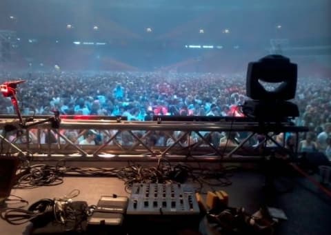 Stage view over packed arena crowd with DJ mixer and lighting rig at Amsterdam dance event production