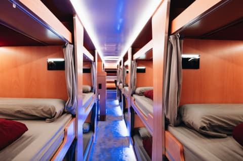 Nightline Sleeperbus interior showing double-stack sleeping berths with curtains and blue ambient lighting