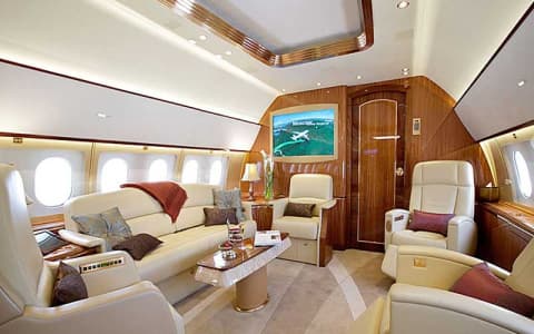 VIP private jet cabin interior with cream leather seating, wood panelling and in-flight entertainment screen