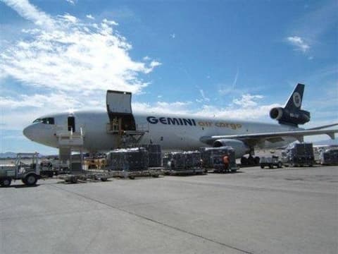 Air cargo aircraft being loaded on the tarmac with freight pallets and ground handling equipment