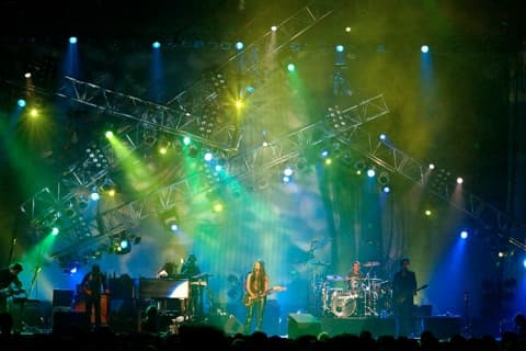 Moving head lighting rig on truss illuminating a live band on stage with green and blue wash